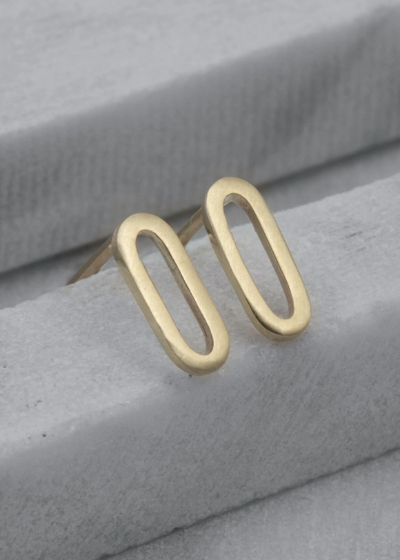 Gold oval stud earrings on a gray fabric background