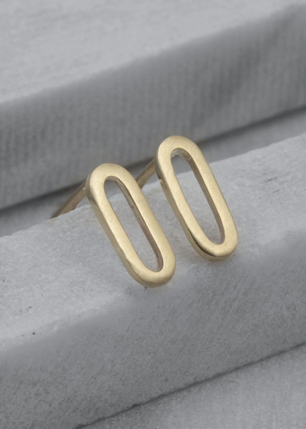 Gold oval stud earrings on a gray fabric background