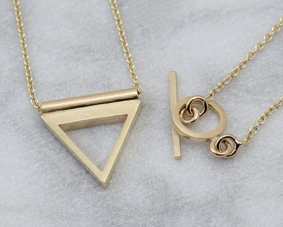 Two gold necklaces with geometric pendants on a light gray background