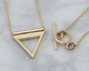 Two gold necklaces with geometric pendants on a light gray background