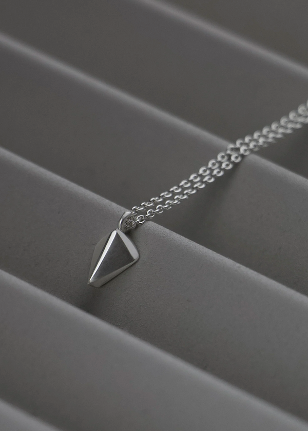 Silver necklace with a triangular pendant on a gray surface