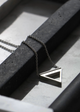 A sterling silver necklace with a geometric triangle symbol on a chain, displayed against a concrete and marble background.