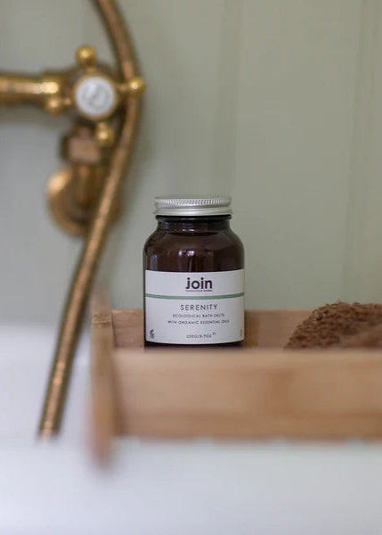 Jar labeled 'join' on a wooden tray with a bathtub and faucet in the background