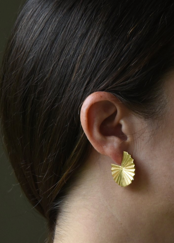 Gold earring worn by a person with dark hair against a neutral background