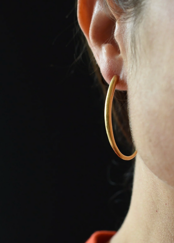 Close-up of a gold hoop earring worn by a person against a dark background