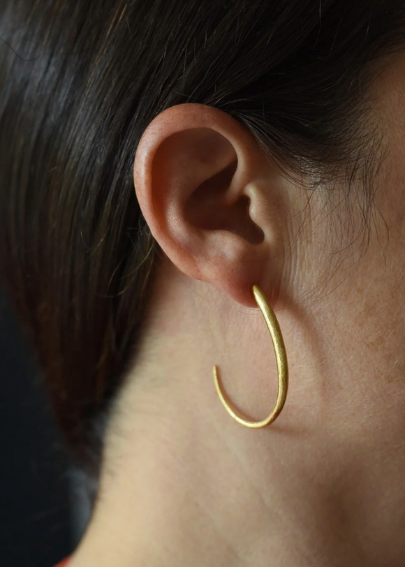 Gold hoop earring worn by a person with dark hair.