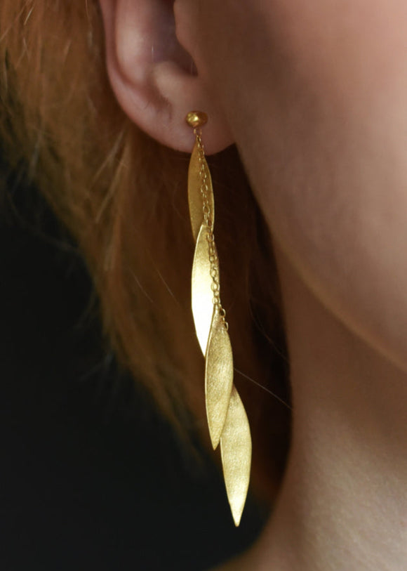 A close-up image of a person wearing gold leaf-shaped earrings that dangle and move with a chain.