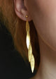 A close-up image of a person wearing gold leaf-shaped earrings that dangle and move with a chain.