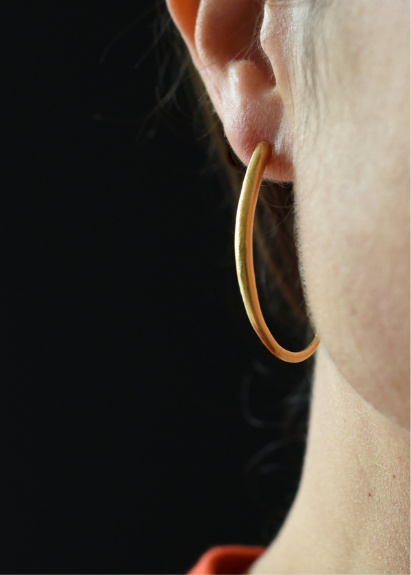 Close-up of a person wearing a gold hoop earring against a dark background
