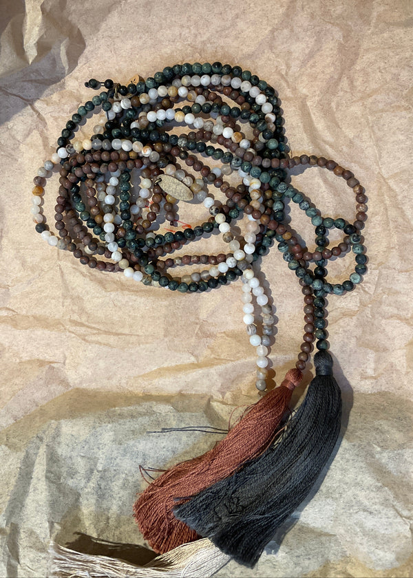A beaded necklace with gray and brown tones, featuring various designs on the beads, laid out on a wooden surface.