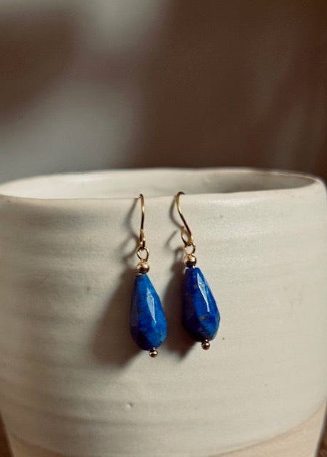 Blue teardrop earrings on a white ceramic surface with a blurred background