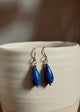 Blue teardrop earrings on a white ceramic surface with a blurred background
