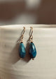 Teal drop earrings with gold hooks on a white ceramic surface