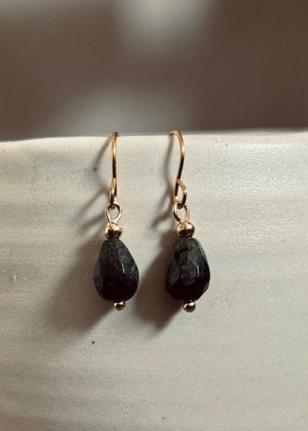 Pair of black teardrop earrings with gold hooks on a light gray surface.
