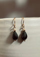 Pair of black teardrop earrings with gold hooks on a light gray surface.