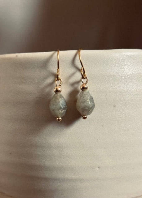 Pair of gold earrings with teardrop-shaped stones on a white surface