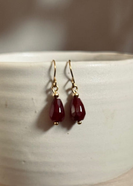 Red teardrop earrings with gold hooks on a white ceramic surface