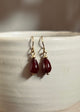 Red teardrop earrings with gold hooks on a white ceramic surface