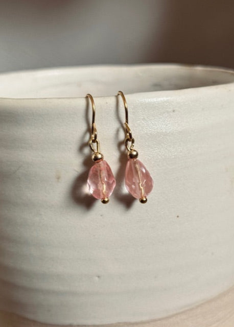 Pink teardrop earrings with gold hooks on a white ceramic surface