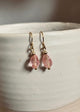 Pink teardrop earrings with gold hooks on a white ceramic surface