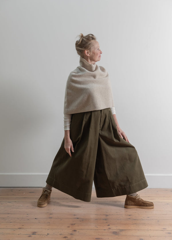 Person wearing a beige sweater and olive green wide-leg pants against a plain background