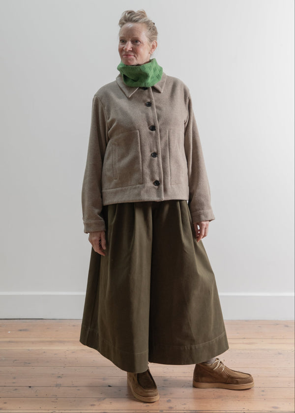 Woman wearing a beige jacket and green scarf against a white wall.