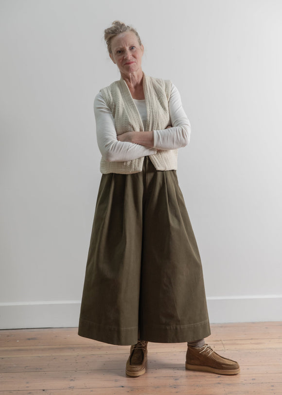 Woman wearing a long beige cardigan over a white shirt and brown skirt on a plain background