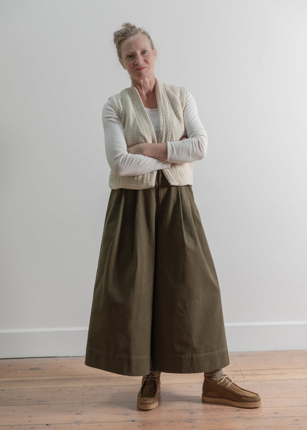 Woman wearing a long beige cardigan over a white shirt and brown skirt on a plain background