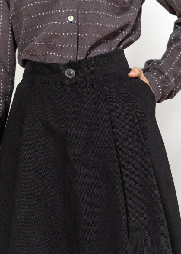 Person wearing a black skirt with a patterned shirt on a white background