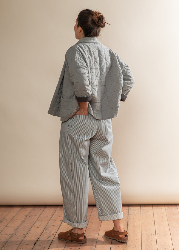 Person wearing a light gray quilted jacket and pants standing against a plain wall.