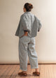Person wearing a light gray quilted jacket and pants standing against a plain wall.