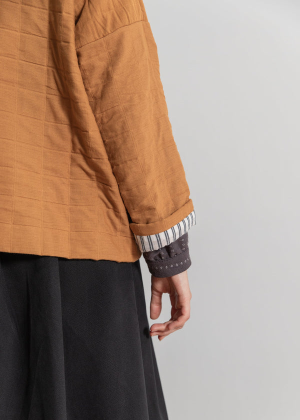 Person wearing a mustard yellow quilted jacket with a gray background