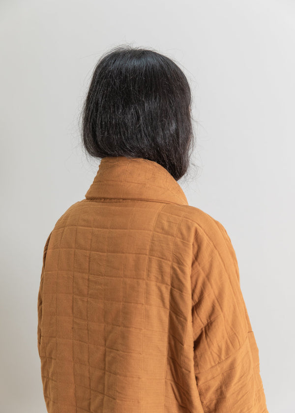 Person wearing a mustard yellow
 quilted jacket against a plain background