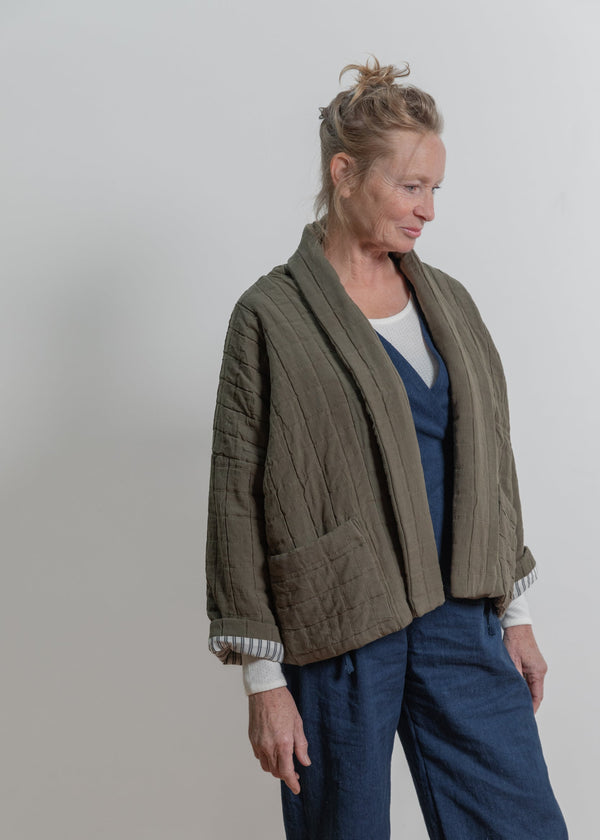 Person wearing a green cardigan over a blue top and pants on a plain background