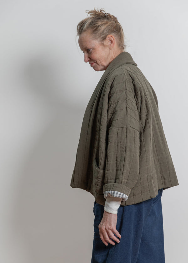 Person wearing a green jacket and blue pants against a plain background