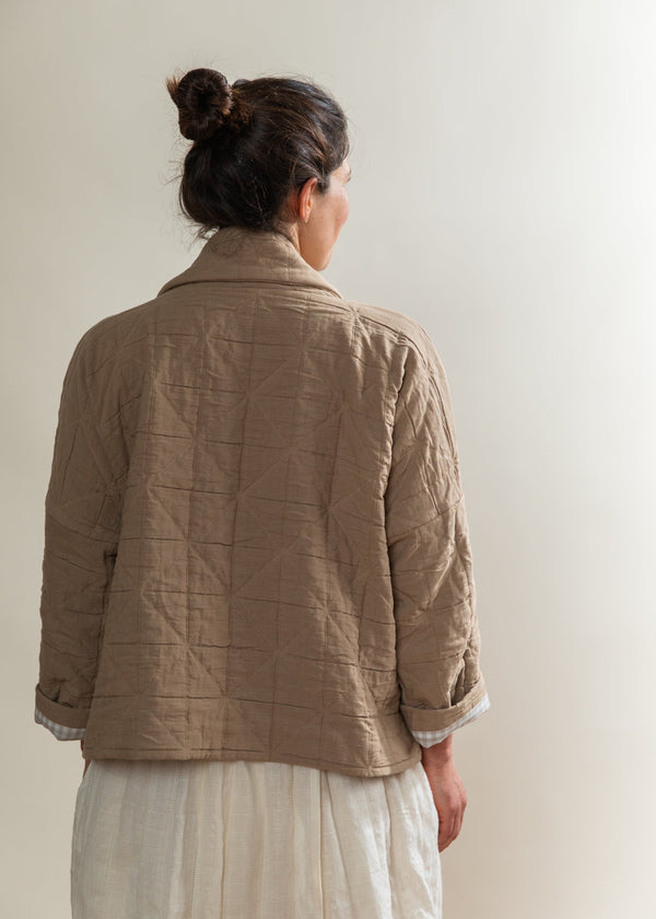 Person wearing a beige quilted jacket against a plain background
