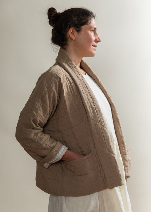 Woman wearing a brown quilted jacket against a plain background