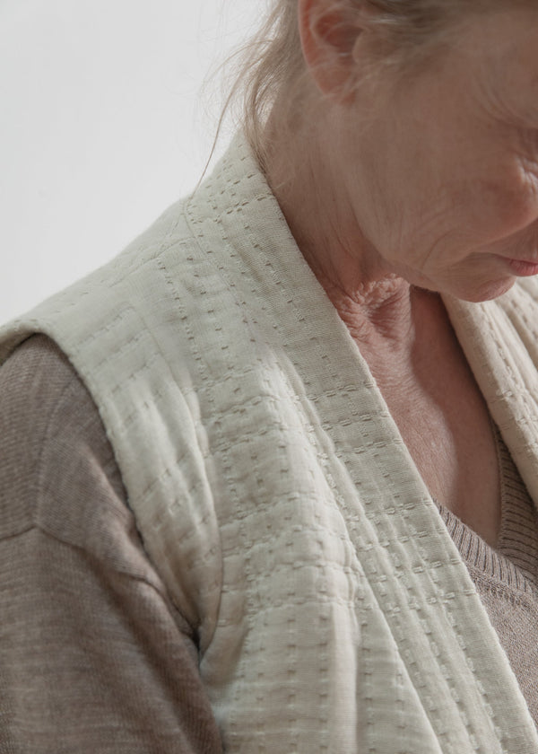Close-up of a person wearing a textured beige vest against a neutral background