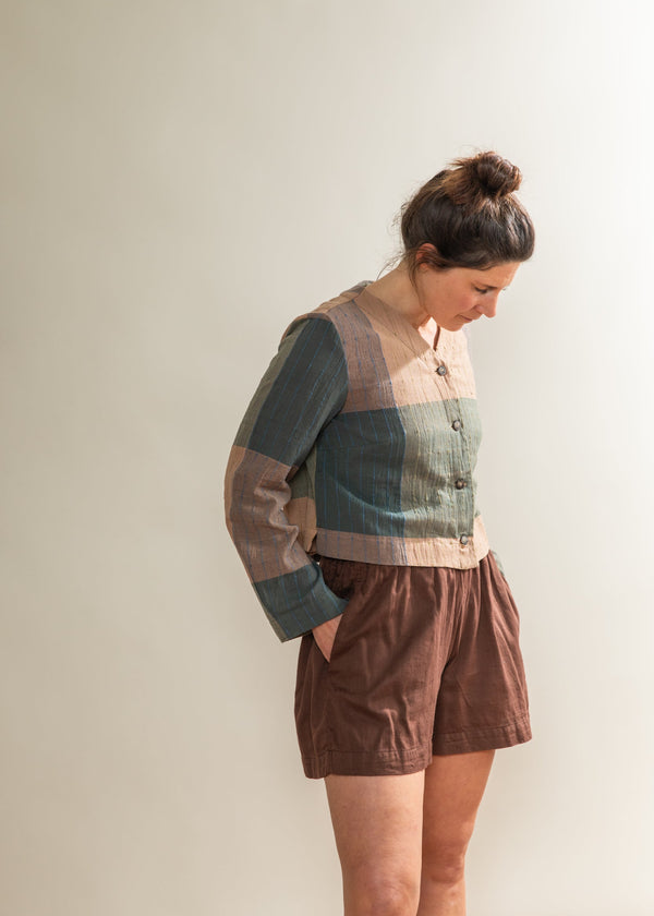 Woman wearing a patchwork sweater and brown shorts against a plain background