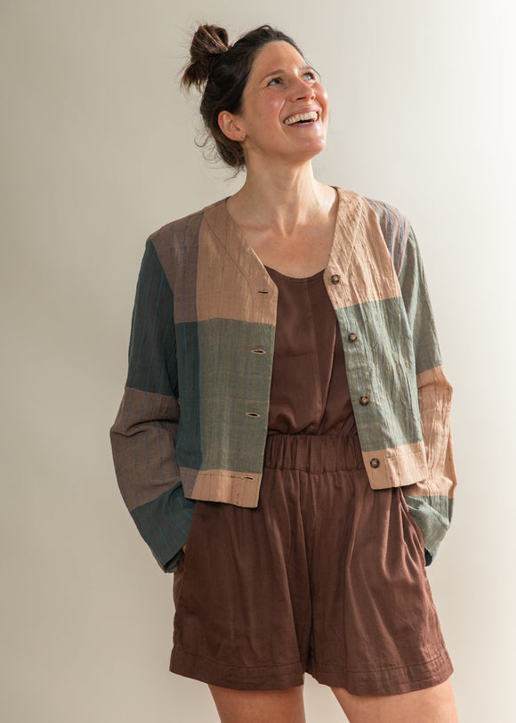 Woman wearing a brown outfit with a plaid jacket against a plain background