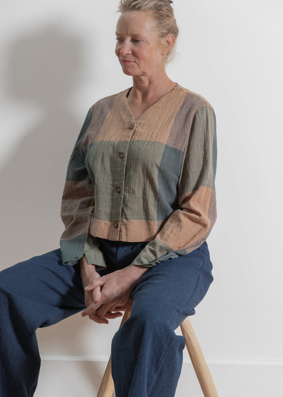 Person wearing a patchwork shirt sitting on a stool against a white wall