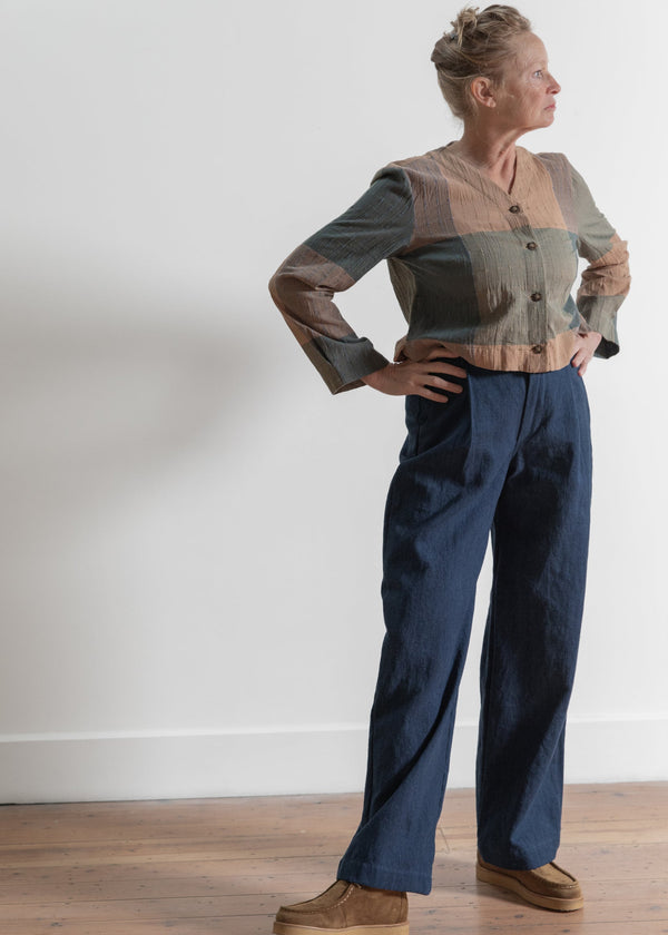 Person wearing a patterned shirt and blue pants standing against a white wall.