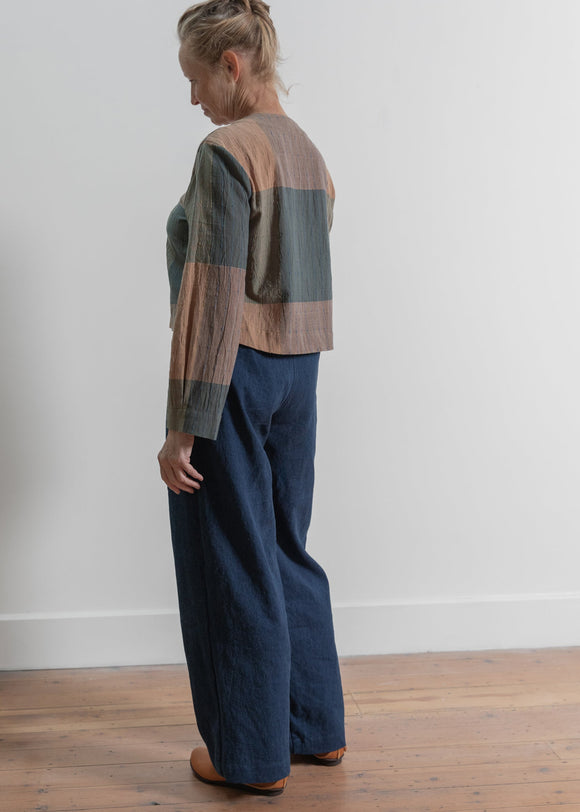 Person wearing a plaid shirt and blue pants standing against a white wall.