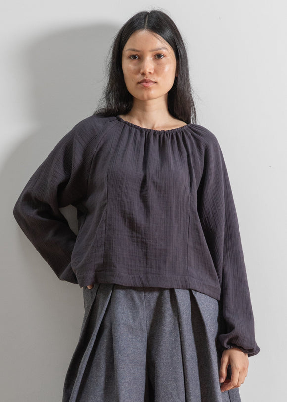 Woman wearing a dark grey blouse and gray skirt against a plain background