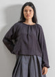 Woman wearing a dark grey blouse and gray skirt against a plain background