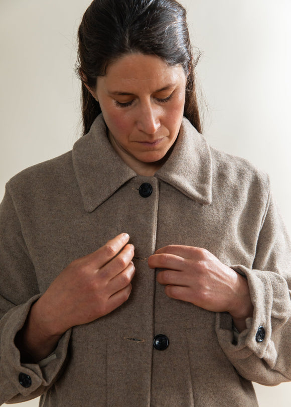 Woman wearing a beige coat with black buttons against a plain background