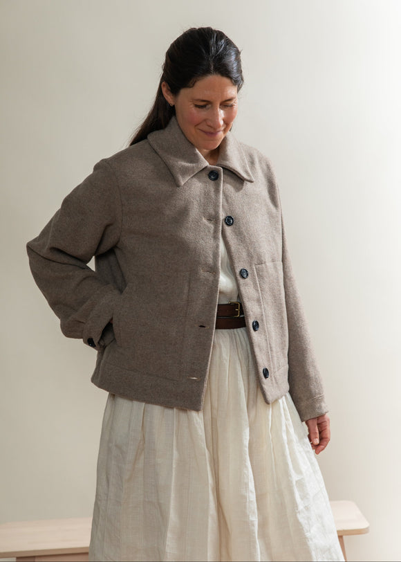 Woman wearing a brown coat and white dress against a plain background