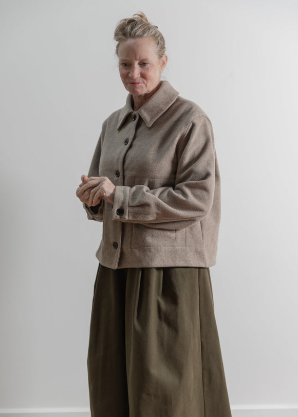 Person wearing a beige coat and green pants against a white background