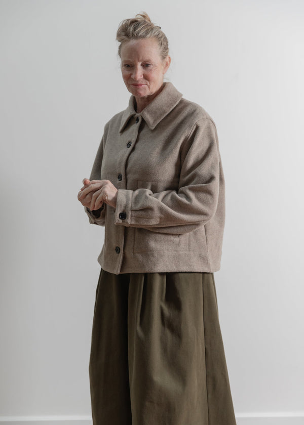 Person wearing a beige coat and green pants against a white background