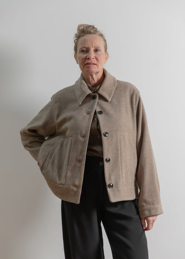 Person wearing a beige jacket against a plain background